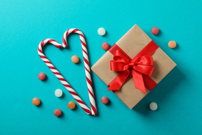 Sweet candy canes and gift box on turquoise background, space for text