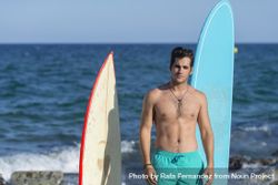 Male surfer standing with boards in front of the water 0gllj5