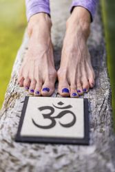 Close up of woman's feet behind an Om sign on a tree trunk over the water.