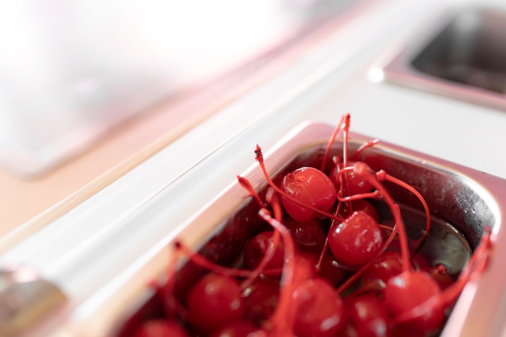 Close up photo of a metal tray filled with cherry toppings on an ice cream parlor counter