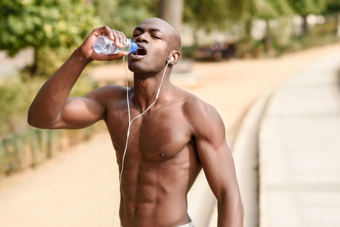 Fit male with shirt off drinking from a water bottle in an outdoor park
