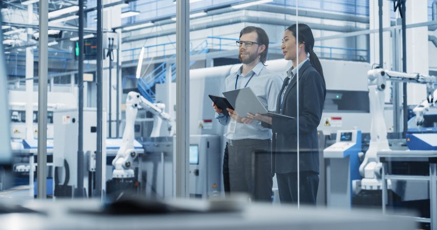 Male Technician and Female Businesswoman Standing in Office, Talking, Using Computers and Monitoring Production at a Modern Automated Electronics Manufacture with AI Robotic Arms