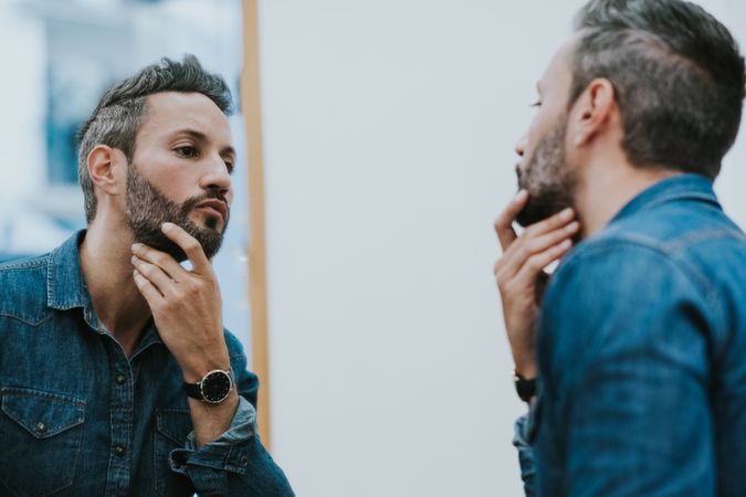 Man looking at mirror and touching beard in salon