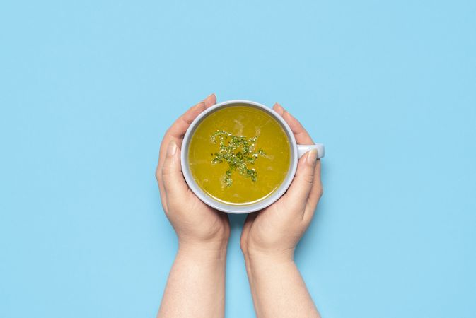 Chicken soup in a mug on a blue table, above view