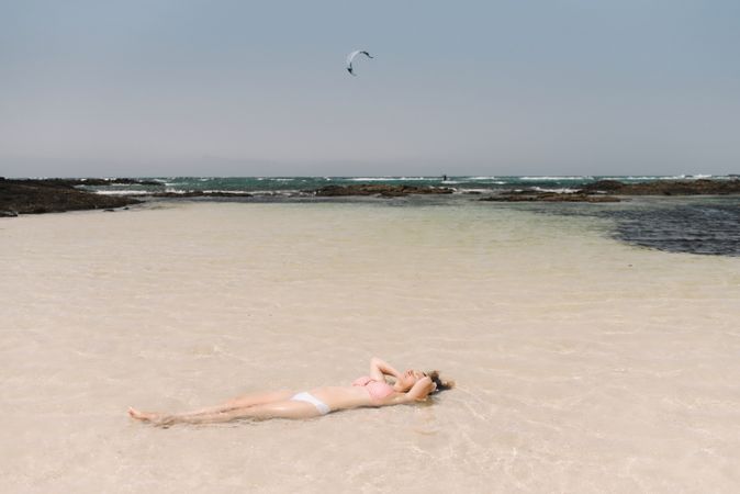 Woman in swimsuit lying in water on seashore