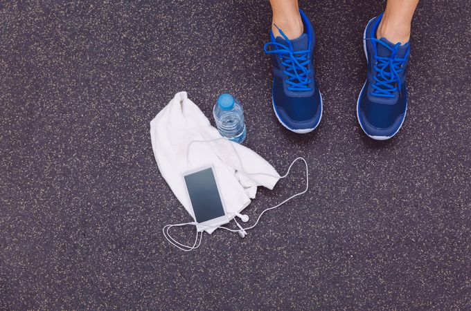Feet of person wearing blue sneakers on gym floor next to towel, phone and water bottle