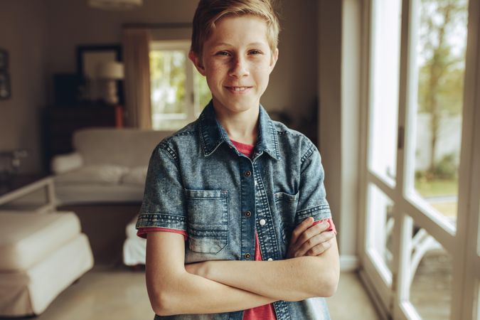 Close up of a smiling boy standing at home with arms crossed