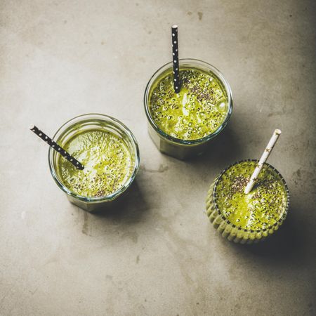 Three green smoothies in glasses with eco friendly straws on concrete background, square crop