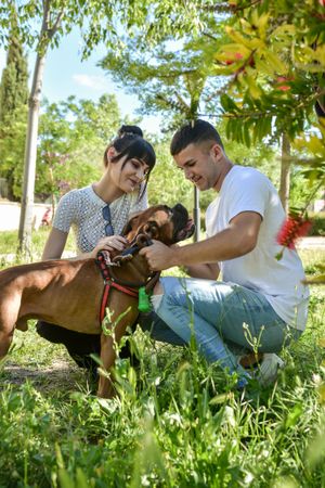 Couple with their dog Boxer sitting in a park .