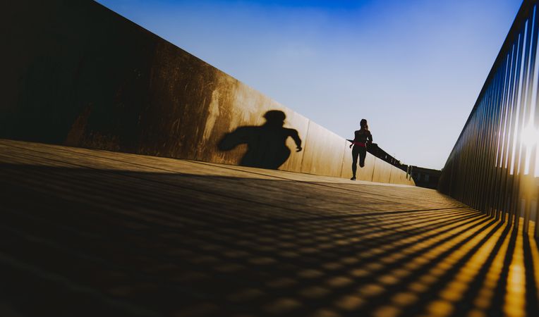 Woman running on walkway in sunny day with blue sky