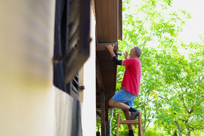 Exterior Repairs in Progress: Man on Ladder Working Under Roof Eaves.