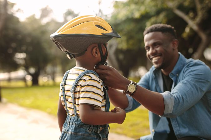 Man helps boy fastens protective helmet for learning to ride bicycle at park