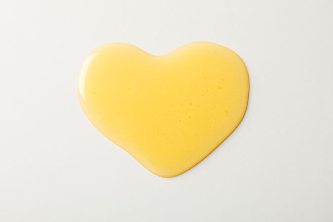 Puddle of honey in shape of heart on neutral background, top view