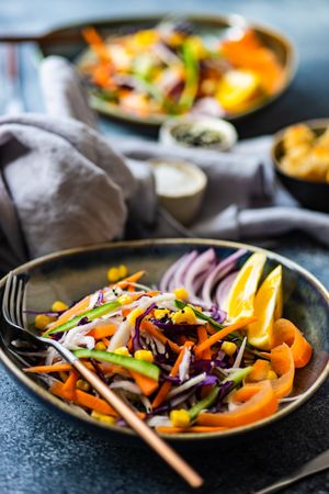 Healthy colorful vegetable salad and lemon slices in bowl on counter with copy space