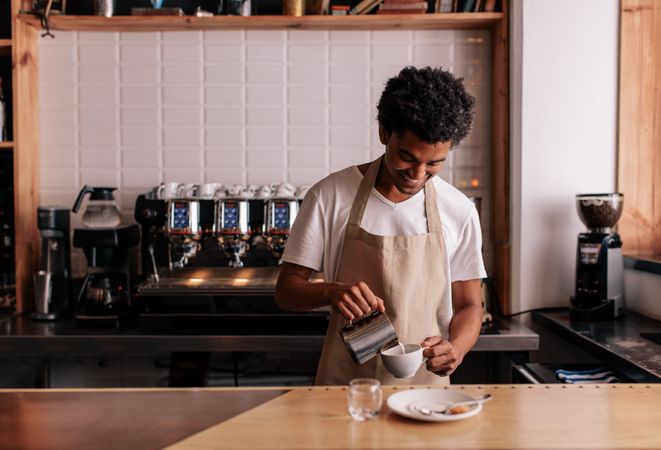 Young man pouring milk into coffee making espresso