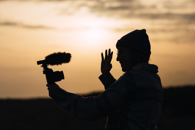 Anonymous happy woman recording vlog on camera under sundown sky