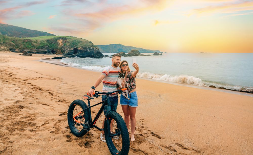 Male and female taking picture with phone standing with bicycle and dog