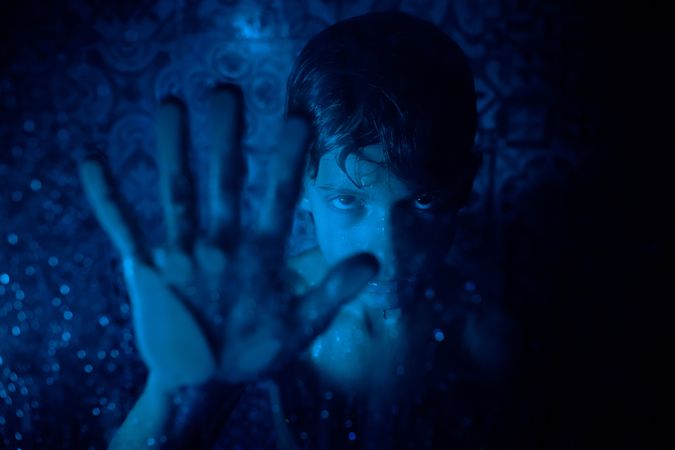 Displeased boy showing stop gesture behind glass wall in bathroo