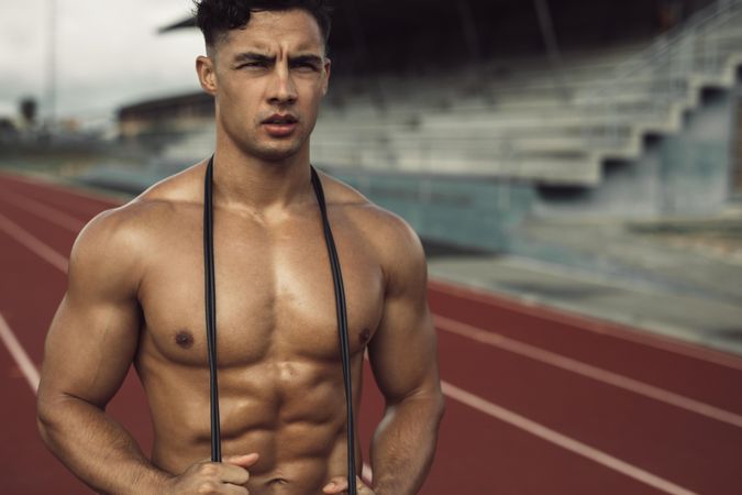 Muscular young man holding jump rope around neck and looking out