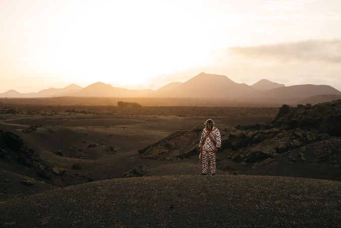 Person in brightly patterned clothes and monster mask standing on volcanic hills in Lanzarote at dusk