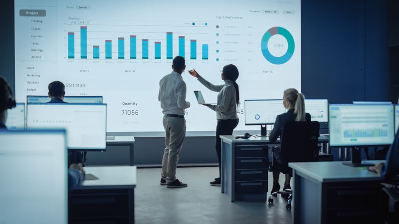 Diverse Team Analyzes Project Data on Large Screen.