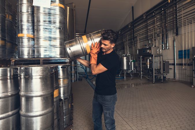 Strong craft brewer lifting beer keg onto shoulder