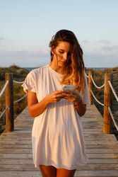 Tanned woman in white shirt walking on bridge and browsing smartphone