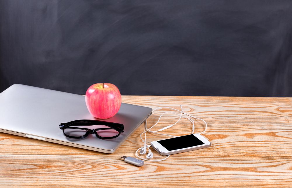 Back to school modern technologies on desk in front of chalkboard