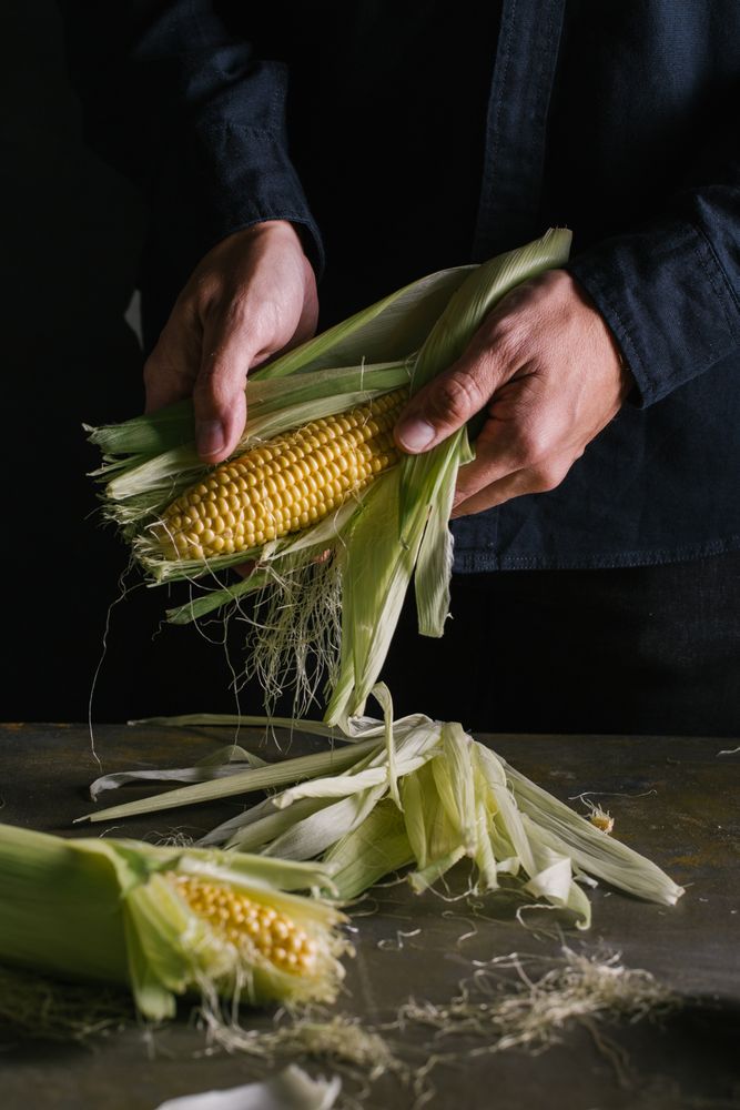 Crop person peeling corn over table