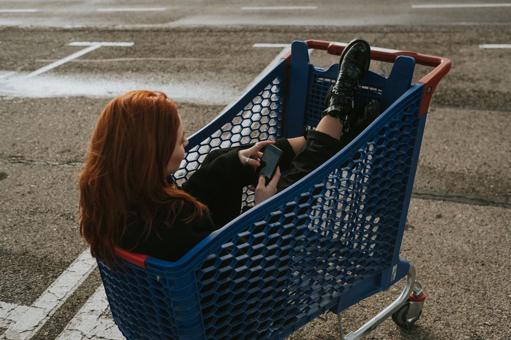Woman with smartphone in shopping trolley in parking lot