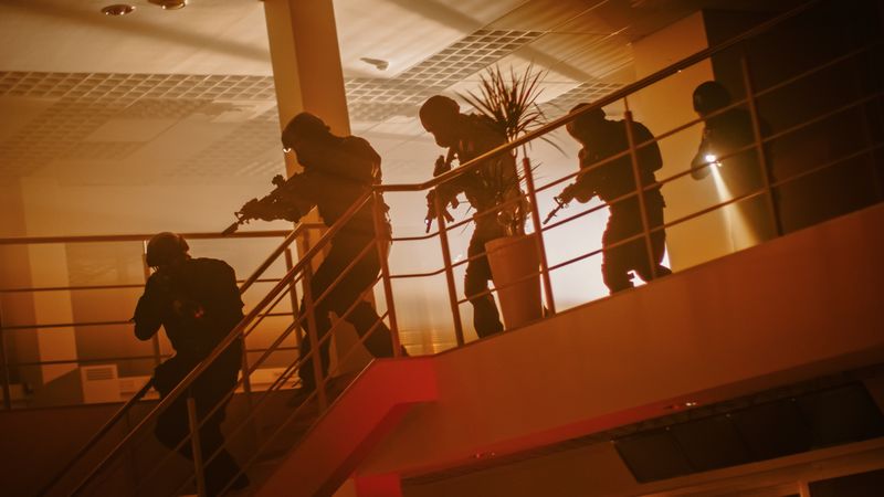 Masked Squad of Armed SWAT Police Officers Run Down the Stairs from a Second Floor in a Dark Office Building.