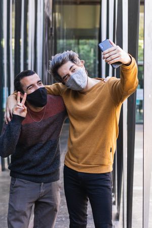 Cheerful men in masks taking selfie in city