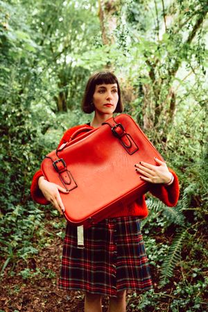 Woman in red with big red suitcase in forest