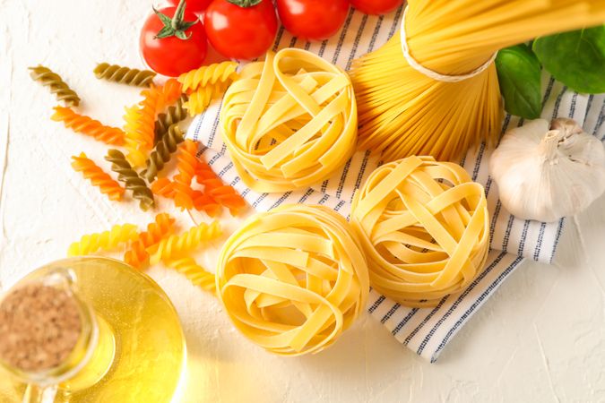 Composition with pasta, tomatoes, garlic, olive oil and kitchen towel on light background, space for text and top view