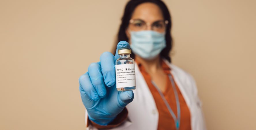 Woman doctor in protective mask and gloves holding a vial with coronavirus vaccine