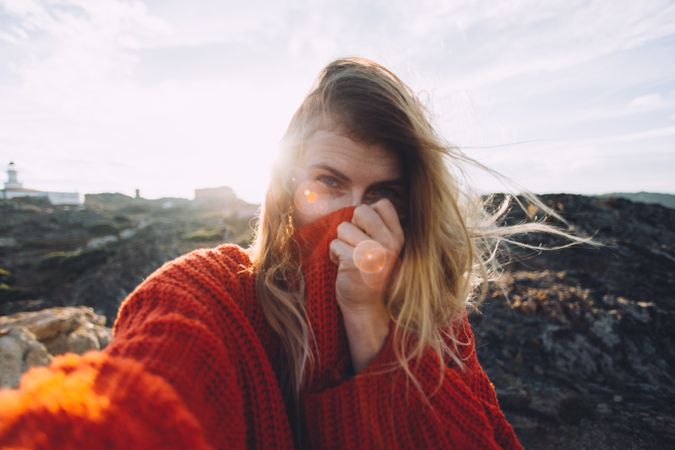 Shy woman in red sweater taking selfie on a hill