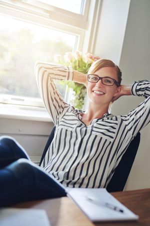 Happy female entrepreneur leaning back and relaxing while working from home office, vertical