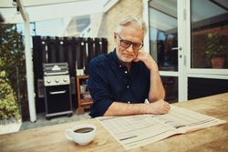 Mature man sitting outside reading a newspaper with coffee