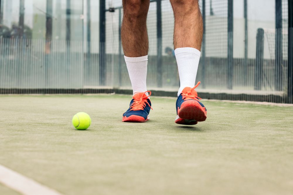 Paddle tennis player close-up photo of the sports shoes and the ball