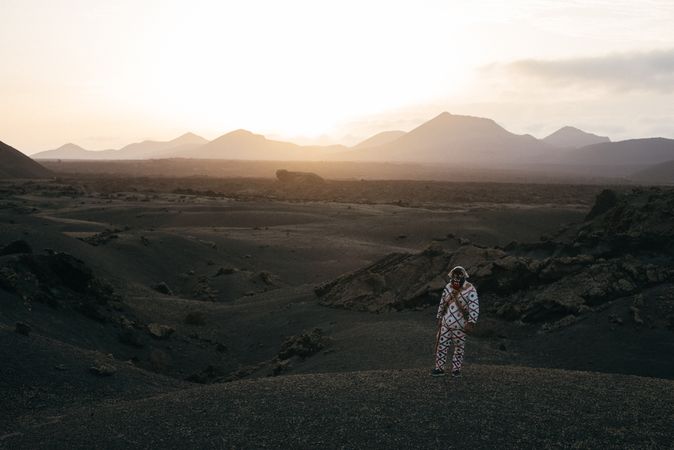 Person in brightly patterned clothes and mask standing on volcanic hills in Lanzarote at dusk