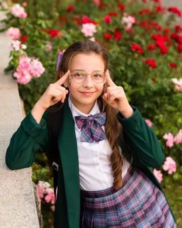 Girl in uniform with both hands adjusting glasses