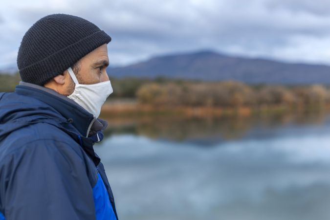 Man in blue jacket and dark beanie looking at lake