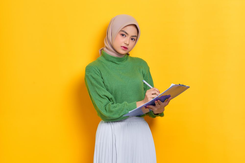 Woman in headscarf writing on clipboard in studio shoot