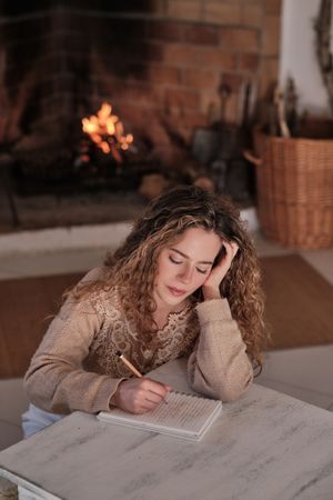 Thoughtful young female writing in diary at home