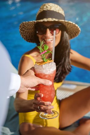 Cheerful woman taking glass of cocktail on poolside