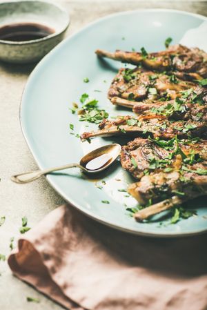 Plate of grilled lamb chops with parsley garnish on light blue plate with copy space