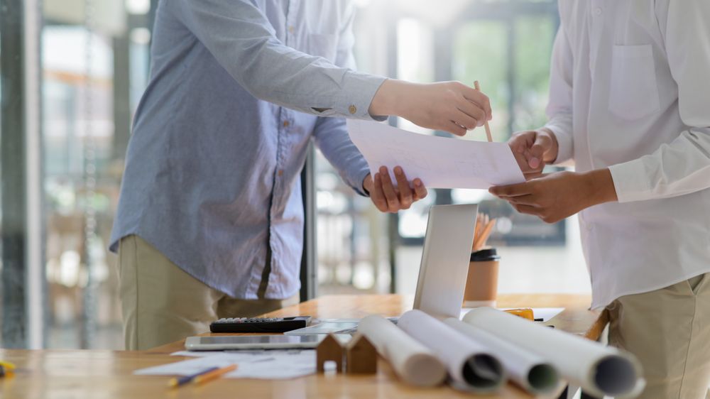 Designer is giving advice on house plans to homeowners, house plans and equipment placed on the drawing table in the office.