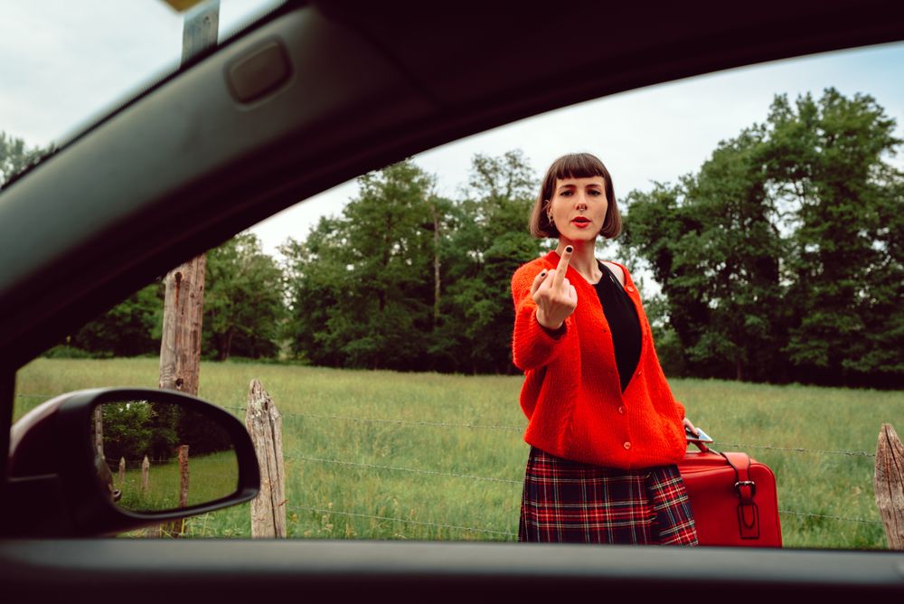 Woman in red sweater gesturing near car on road