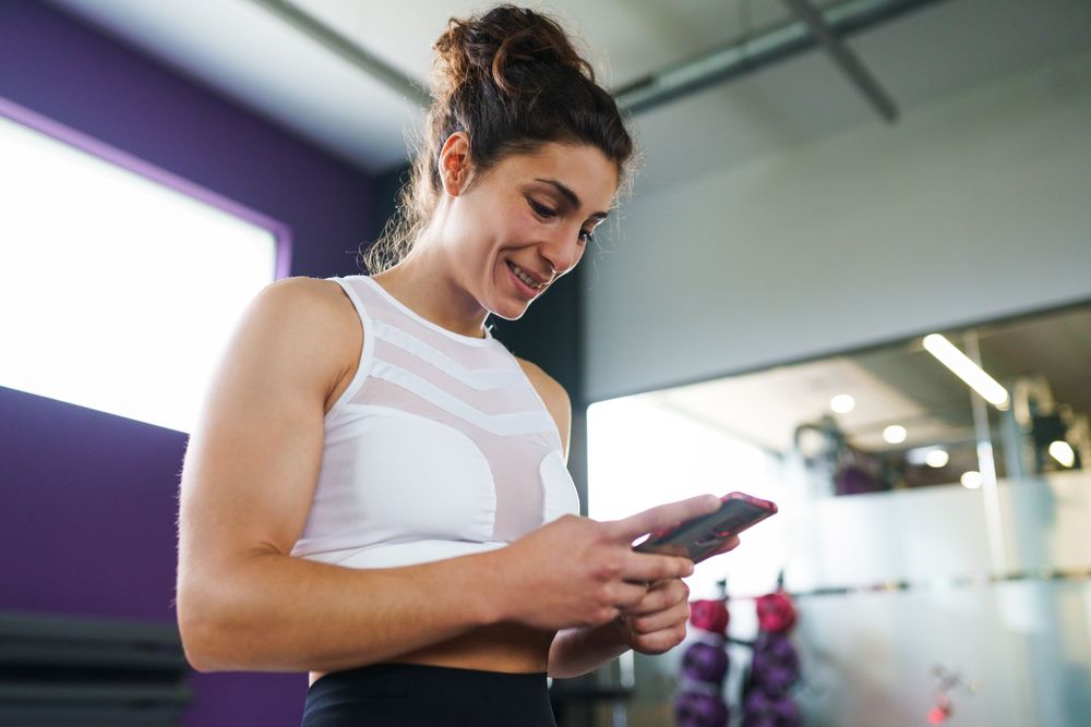 Woman looking down and smiling at her smart phone in gym