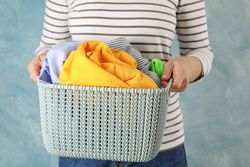 Young woman hold basket with clean clothes, space for text